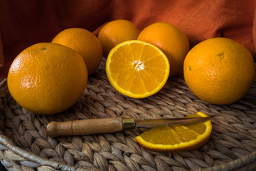 Hermosas naranjas para zumo preparadas con mantel naranja y cuchillo de mango de madera sobre bandeja de ratan.