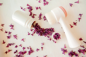 White jar with lilac petals on a white background, facial massager, alternative medicine and skin care.