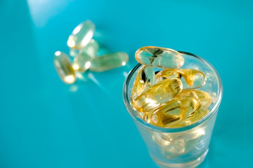 A handful of omega 3 capsules with a glass beaker on a blue background.