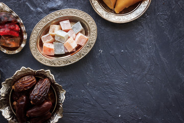 Top view of traditional Turkish and Arab desserts on rustic blue background. Turkish delight, palm date and dried fruit pulp in silver bowls. Ramadan culture concept with cpy space.