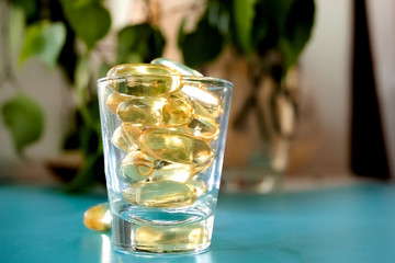 A glass cup with omega 3 vitamins stands on a blue table near the window, near a birch tree,.