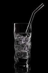 Glass of sparkling water soda drink with ice on black background