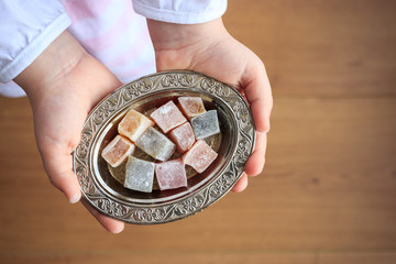 Top view of colorful Turkish delight in silver bowl on the little girl hands. Traditional ramadan holiday in Turkey. Turkish culture concept.