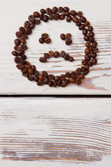 Unhappy smiley face made of coffee beans. Bad tastless coffee concept. White wooden planks on background.