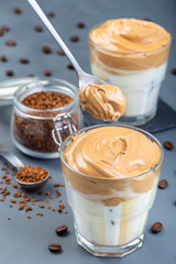 Trendy korean drink Dalgona coffee with ice, spoon put coffee foam, dark gray background, vertical