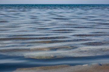 The surface is salty sea water, swaying in small waves near the shore, through the transparent bottom you can see stones and pebbles
