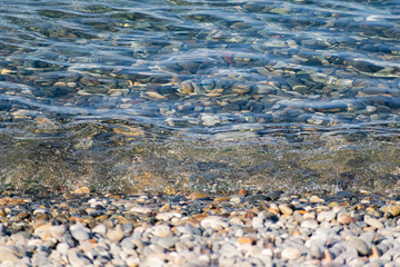 The surface is salty sea water, swaying in small waves near the shore, through the transparent bottom you can see stones and pebbles
