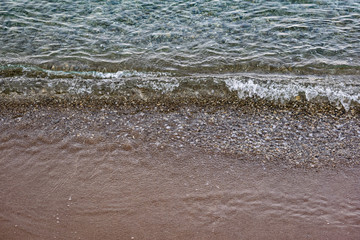The surface is salty sea water, swaying in small waves near the shore, through the transparent bottom you can see stones and pebbles
