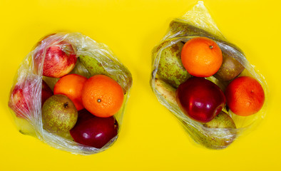 Ecology concept: fruits (oranges, pears, apples) in two plastic bags on yellow backround. Top veiw.
