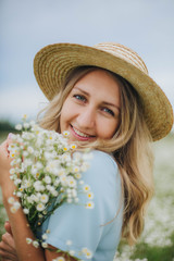 beautiful blonde girl in a field of daisies. woman in a blue dress in a field of white flowers. girl with a bouquet of daisies. summer tender photo in the village. wildflowers. girl in a straw hat