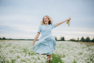 beautiful blonde girl in a field of daisies. wreath of wildflowers on his head. woman in a blue dress in a field of white flowers. charming girl with a bouquet of daisies. summer tender photo