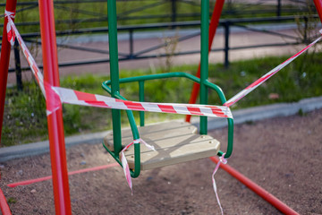 The playground is in quarantine due to the coronavirus pandemic. Warning Red and white ribbons are torn by bad citizens on a swing.