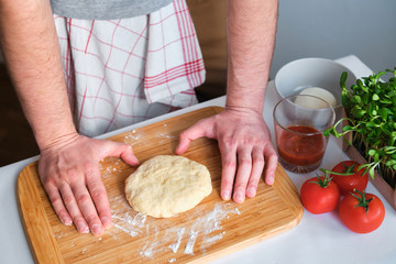 A man is preparing pizza dough. Men's hands in flour. Cooking homemade italian pizza. Preparation raw ingredients for baking. Fresh natural healthy food. Сulinary сhef kneading dough on kitchen table