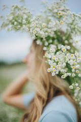 Naklejka premium beautiful blonde girl in a field of daisies. wreath of wildflowers on his head. woman in a blue dress in a field of white flowers. charming girl with a bouquet of daisies. summer tender photo