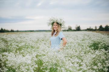 Fototapeta na wymiar beautiful blonde girl in a field of daisies. wreath of wildflowers on his head. woman in a blue dress in a field of white flowers. charming girl with a bouquet of daisies. summer tender photo