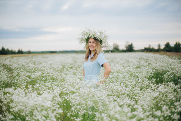 beautiful blonde girl in a field of daisies. wreath of wildflowers on his head. woman in a blue dress in a field of white flowers. charming girl with a bouquet of daisies. summer tender photo