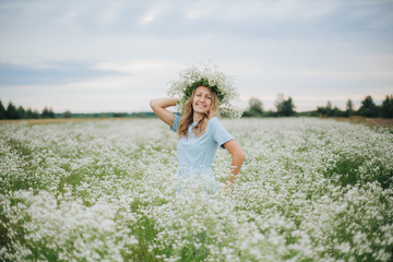 Fototapeta na wymiar beautiful blonde girl in a field of daisies. wreath of wildflowers on his head. woman in a blue dress in a field of white flowers. charming girl with a bouquet of daisies. summer tender photo