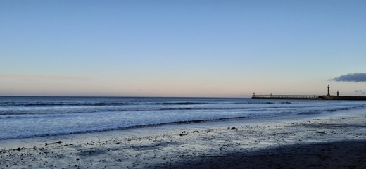 Sandy beach view with waves at sunset in Whitby, North Yorkshire