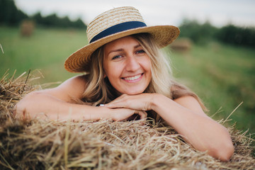 beautiful girl in a straw hat on a field with straw bales. girl sitting on the hay. blonde in the summer in a field with a hat. life in the countryside, outdoors. eco project. clean environment