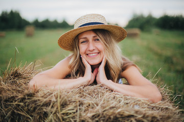 beautiful girl in a straw hat on a field with straw bales. girl sitting on the hay. blonde in the summer in a field with a hat. life in the countryside, outdoors. eco project. clean environment