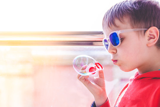 blond kid with sunglasses playing with soap bubbles near balcony