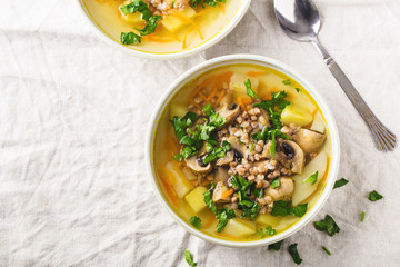 Soup of mushrooms, buckwheat, potatoes and carrots with herbs in bowls, light background, horizontal format. Space for text