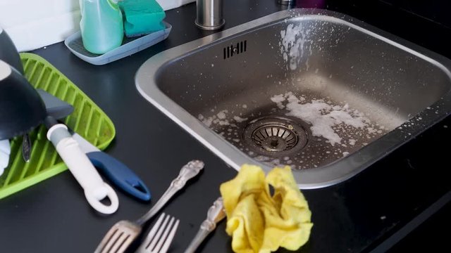 Washing dishes by hand, a young woman without gloves washes knives and other Cutlery in the sink