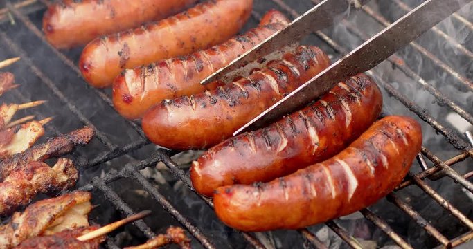 Hot tasty grilled sausages frying on smoking barbecue. Slow motion video