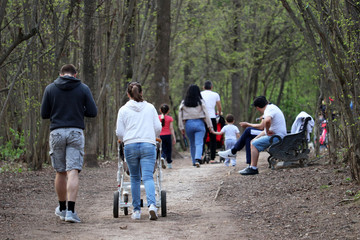 People walking in a spring park, couple with baby carriage in the foreground. Quarantine in a city during covid-19 coronavirus pandemic, violation of social distance during may holidays