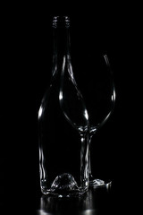 Empty transparent bottle silhouette with wine glass behind. The background is black