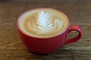 A cup of coffee or cappuccino. A beautiful red cup stands on a wooden table. Fluffy milk froth close up. Breakfast in a rural hotel.