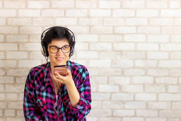 A young brunette woman listens to music through headphones from a smartphone. Talking on the phone on Skype. Stay at home. Meditation with music. Background with Copy space. Toned