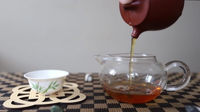 Chinese puer tea is poured from a clay teapot into a glass bowl