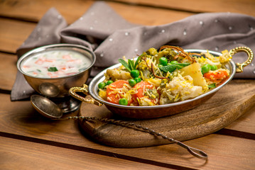 Biryani indian cuisine in bowl with vegetables rice traditional wooden board texture