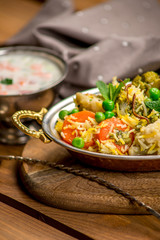 Biryani indian cuisine in bowl with vegetables rice traditional wooden board texture