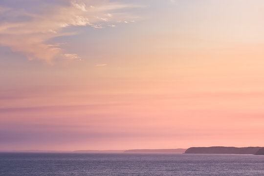 Ethereal pastel coloured sunset on the sea, with cliffs in the background . Concept of reflection and nature. Algarve, Portugal