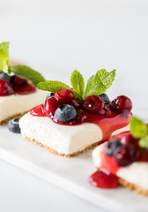 A close up vertical view of a row of cherry cheesecake squares garnished with berries and mint.