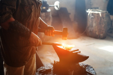 Manual work of a blacksmith in a blacksmith Shop. Hammer blows on the iron billet on the anvil. Forging sword blades is a retro weapon - obrazy, fototapety, plakaty