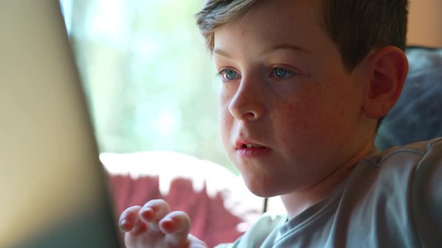 Move from of child&rsquo;s face  to hands doing schoolwork at home on laptop