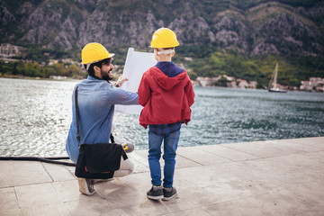 Harbor engineer with his son holding the paper, construction work, smiling.