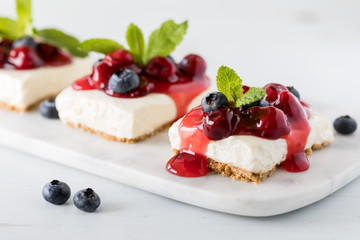 A close up view of cheesecake squares topped with cherry sauce and blueberries and garnished with mint.