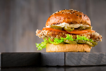 Tasty burger with beef, tomato, pickled, onion, jalapeno pepper, lettuce and sauce on wooden board on wooden background