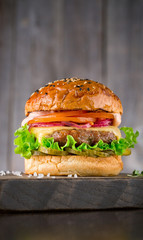 Tasty burger with beef, tomato, pickled, onion, cheese, lettuce and sauce on wooden board on wooden background