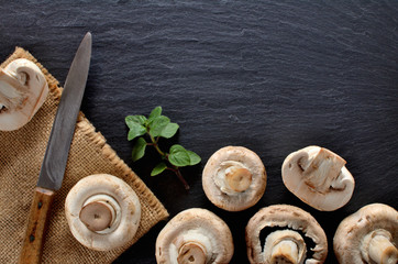 Edible half pieced mushrooms - champignons, sprig of thyme and rustic knife on vintage slate slab. Copyspace. View from above.