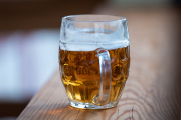 a big glass of beer on a wooden bar and a man's hand, close up