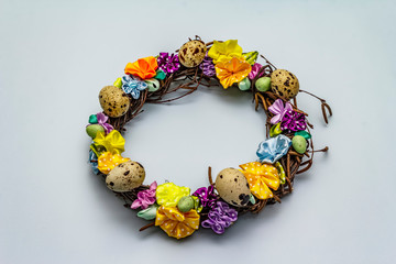 Hand crafted Easter wicker wreath with quail eggs and handmade flowers. Birch branches, polka dot satin ribbon. Stay at home concept. Festive Easter background