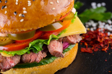 Tasty burger with cutting beef, tomato, pickled, onion, lettuce and sauce on black plate