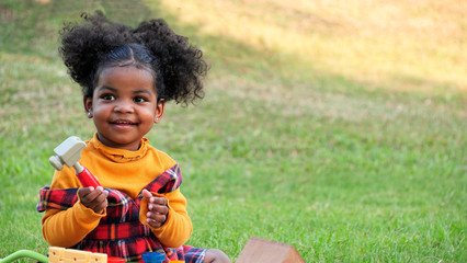 Adorable African girl enjoys to playing her toys in park or garden during a picnic with her family.