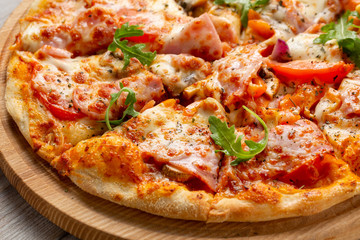 Tasty pizza with ham, mushrooms, tomatoes and arugula on wooden cutting board on white background.