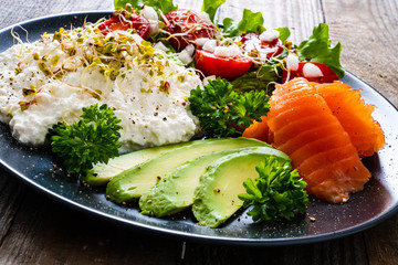 Breakfast - smoked salmon, cottage cheese, avocado and vegetable salad on wooden table
